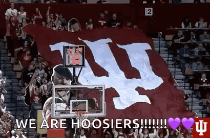 A Man Is Holding A Basketball Hoop In Front Of A Large Banner That Says We Are Hoosier ! GIF