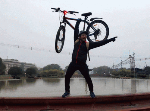 A Man Is Holding A Bicycle Over His Head And Pointing At The Camera GIF