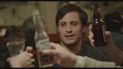 a man is holding a bottle of beer and a bottle of tequila while a group of people toast him .