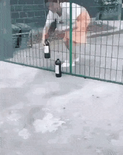 A Man Is Holding A Bottle Of Wine In Front Of A Fence GIF