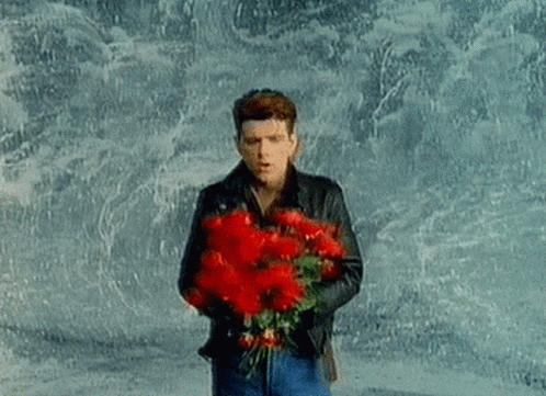 A Man Is Holding A Bouquet Of Red Flowers In His Hands . GIF