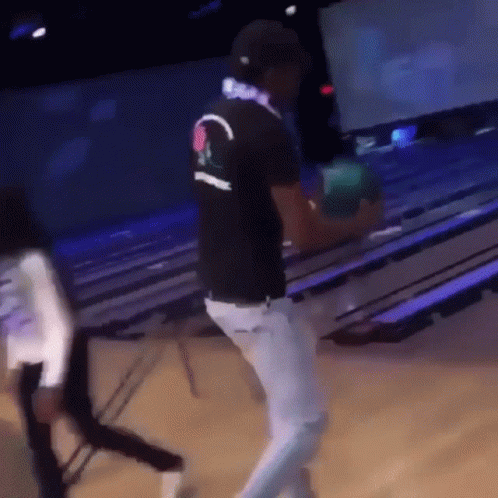 A Man Is Holding A Bowling Ball In A Bowling Alley While Wearing Headphones GIF