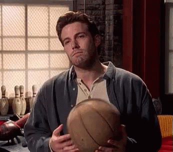 A Man Is Holding A Bowling Ball In His Hands In Front Of Bowling Pins . GIF