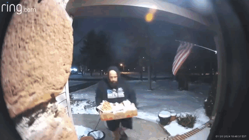 A Man Is Holding A Box Of Pizza In Front Of A Ring Doorbell . GIF