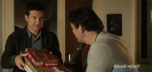 A Man Is Holding A Box Of Scrabble While Another Man Holds A Box Of Pizza . GIF