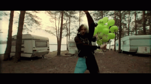 A Man Is Holding A Bunch Of Green Balloons With A Sticker That Says ' A ' On It GIF