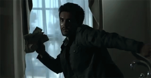 A Man Is Holding A Bunch Of Money In His Hand While Looking Out Of A Window . GIF