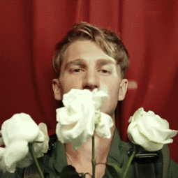 A Man Is Holding A Bunch Of White Roses In Front Of His Mouth GIF