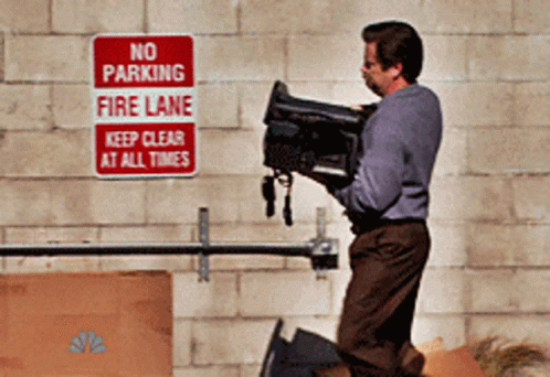 A Man Is Holding A Camera In Front Of A No Parking Fire Lane Sign GIF