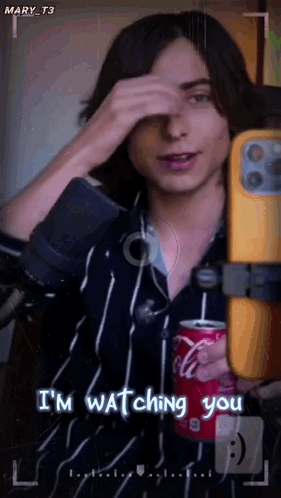 a man is holding a can of coca cola while taking a picture of himself .