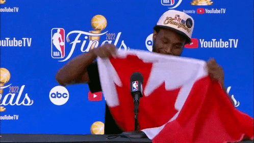 A Man Is Holding A Canadian Flag In Front Of A Microphone GIF
