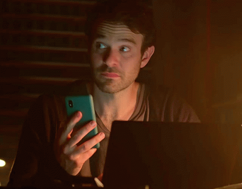 A Man Is Holding A Cell Phone In Front Of A Laptop Computer GIF