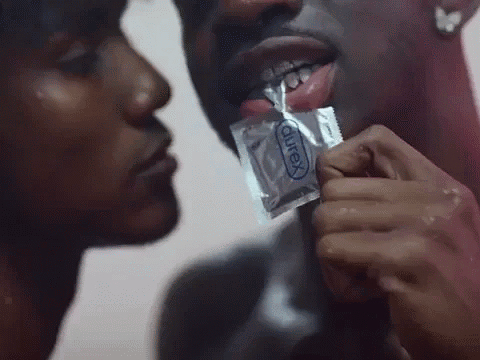 A Man Is Holding A Condom In His Mouth While A Woman Kisses Him GIF
