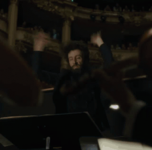 A Man Is Holding A Conductor 'S Baton In His Hands In A Dark Room GIF