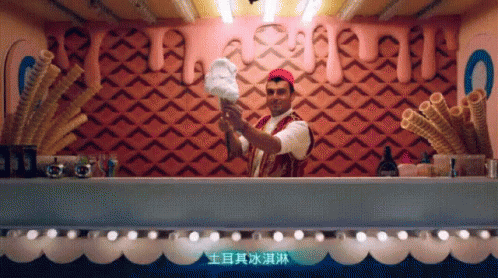 A Man Is Holding A Cotton Candy Cone In Front Of A Wall With Chinese Writing GIF