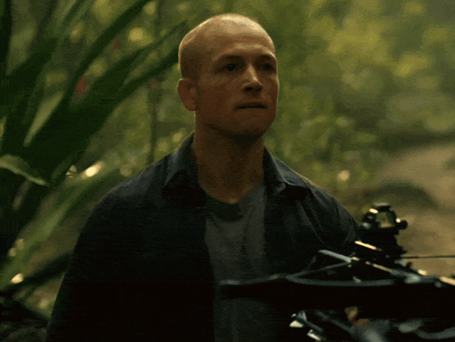 A Man Is Holding A Crossbow In The Woods And His Mouth Is Open GIF
