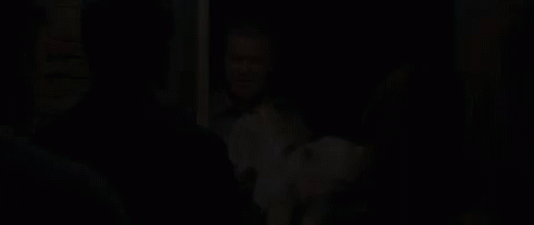 A Man Is Holding A Dog In His Arms While Standing In Front Of A Group Of People In A Doorway . GIF