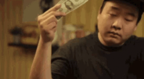 A Man Is Holding A Dollar Bill In His Hand And Looking At It . GIF