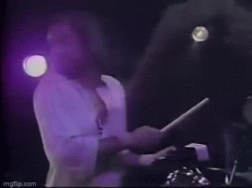 A Man Is Holding A Drum Stick In His Hand On A Stage . GIF
