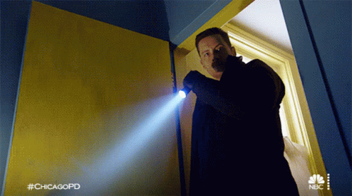 A Man Is Holding A Flashlight In A Doorway With #Chicagopd Written On The Bottom GIF
