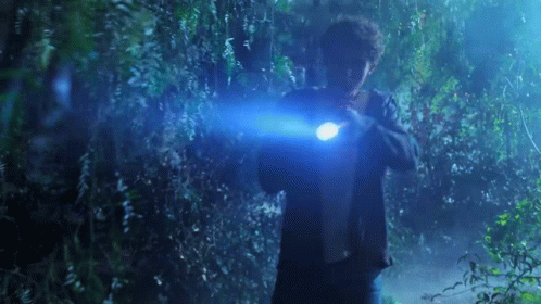 A Man Is Holding A Flashlight In His Hand In A Dark Forest . GIF