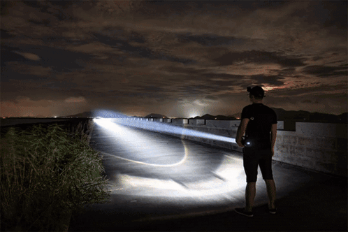 A Man Is Holding A Flashlight While Standing On A Bridge GIF