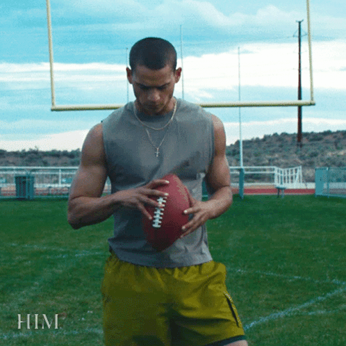 A Man Is Holding A Football On A Field And The Word Him Is On The Bottom GIF