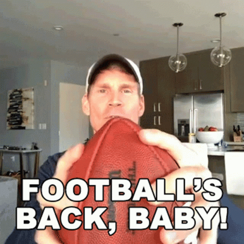 A Man Is Holding A Football With The Words " Football 'S Back Baby " Written On It GIF