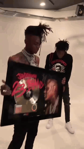 A Man Is Holding A Framed Picture Of A Man With Dreadlocks And The Word Tomorrow On It GIF