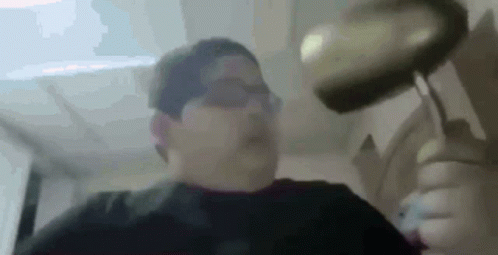 A Man Is Holding A Frying Pan Over His Head In A Blurry Photo . GIF