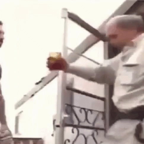 A Man Is Holding A Glass Of Beer And A Knife In Front Of A Building . GIF