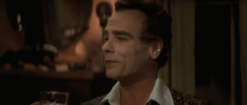 A Man Is Holding A Glass Of Beer In His Hand GIF