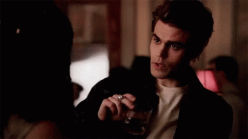 a man is holding a glass of wine and smoking a cigarette while talking to a woman .