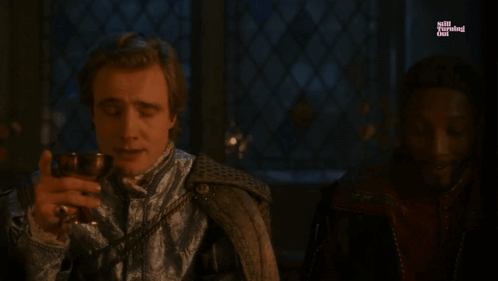 A Man Is Holding A Glass Of Wine And The Word Agony Is On The Screen Behind Him GIF