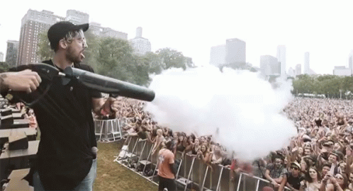 A Man Is Holding A Gun In Front Of A Crowd At A Concert GIF