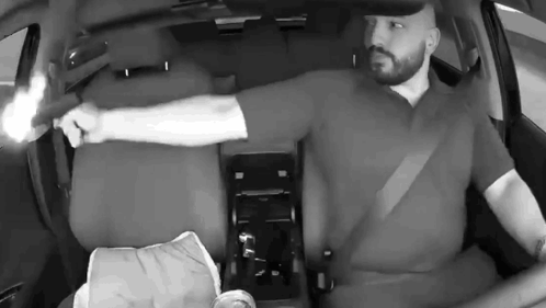 A Man Is Holding A Gun In His Hand While Sitting In A Car . GIF
