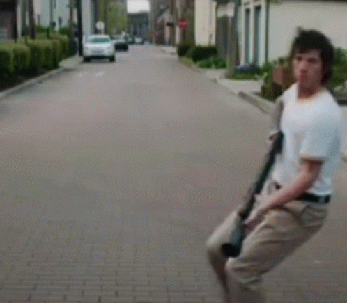A Man Is Holding A Gun While Walking Down A Brick Street . GIF
