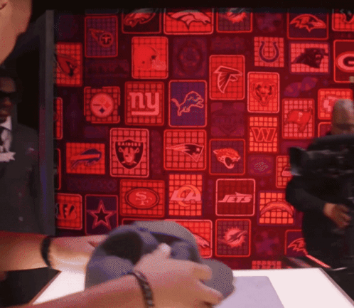 a man is holding a hat in front of a wall with logos for the new york jets and new york raiders