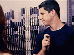 A Man Is Holding A Hockey Stick In Front Of A Wall Of Hockey Sticks GIF