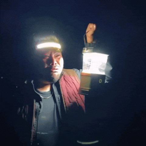 A Man Is Holding A Lantern In His Hand And Wearing A Headlamp GIF