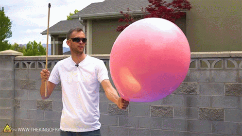 A Man Is Holding A Large Pink Balloon In Front Of A Brick Wall GIF