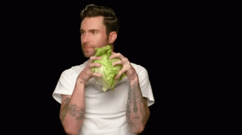 A Man Is Holding A Lettuce Head In Front Of His Mouth . GIF