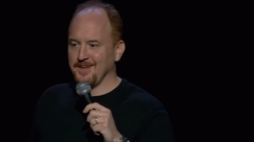 A Man Is Holding A Microphone And Making A Funny Face While Standing On A Stage . GIF