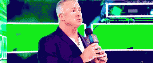 A Man Is Holding A Microphone In Front Of A Green Background . GIF