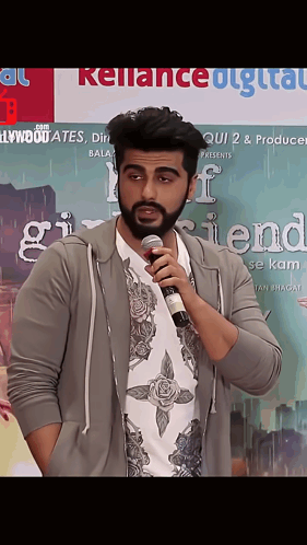 A Man Is Holding A Microphone In Front Of A Poster For Girlfriend GIF