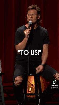 A Man Is Holding A Microphone In Front Of A Red Curtain And Talking Into It . GIF
