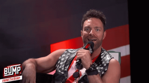 A Man Is Holding A Microphone In Front Of A Sign That Says " Bump " GIF