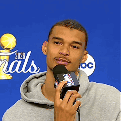 A Man Is Holding A Microphone In Front Of A Sign That Says Finals 2026 GIF