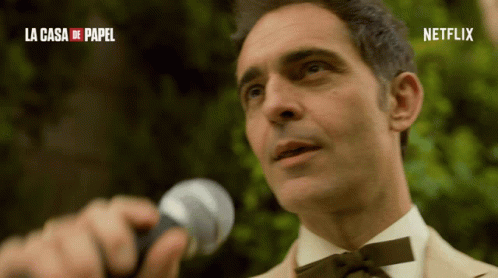 A Man Is Holding A Microphone In Front Of A Sign That Says Netflix GIF