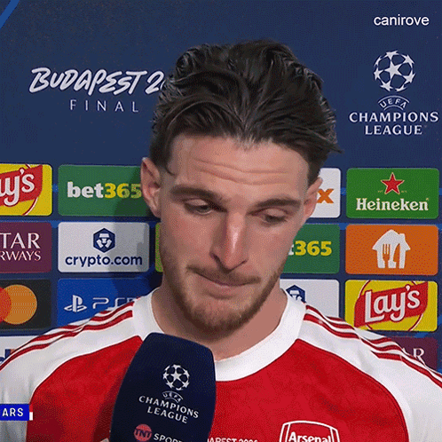 A Man Is Holding A Microphone In Front Of A Uefa Champions League Logo GIF